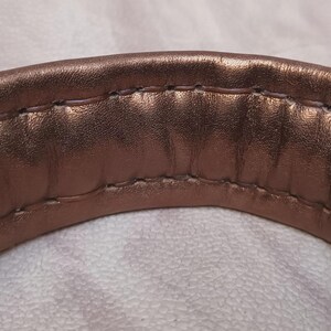 May include: Close-up of a brown leather strap with a stitched seam. The strap is curved and appears to be part of a bag or purse.