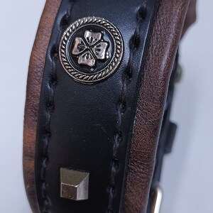 May include: A black leather bracelet with brown leather trim, silver studs, and a silver clover charm.
