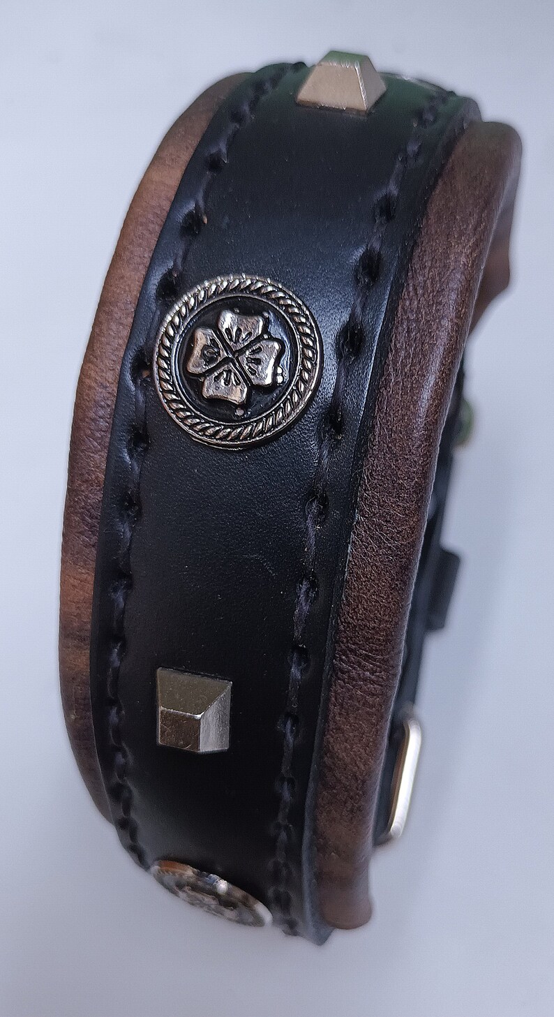 May include: A black leather bracelet with brown leather trim, silver studs, and a silver clover charm.