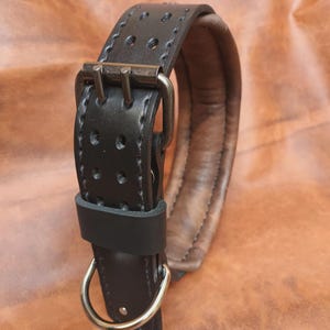 K&ouml;nnte beinhalten: Schwarzes Lederhundekragen mit gepolstertem Futter und einer silbernen Schnalle. Das Halsband hat einen D-Ring zum Anbringen einer Leine.