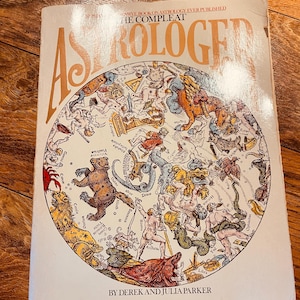 May include: A vintage book titled "The Compleat Astrologer" with a cream-colored cover. The cover features a detailed, colorful illustration of astrological symbols and figures within a circular design. The book is by Derek and Julia Parker.