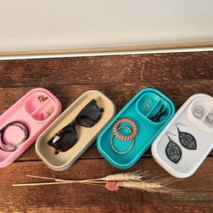 May include: Four different colored silicone trays with compartments for storing jewelry and accessories. The trays are pink, beige, teal, and white.