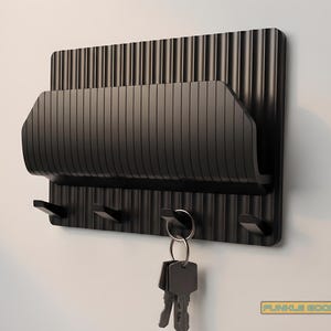 Peut inclure: Un porte-clés mural noir avec un porte-courrier ou un porte-téléphone intégré. Le porte-clés comporte trois crochets et une fente pour le courrier. Un jeu de clés est suspendu à un porte-clés sur l'un des crochets. Le porte-clés est en matériau strié.