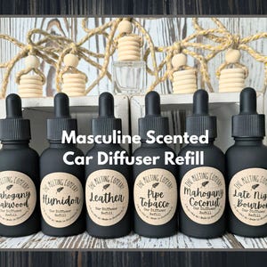 May include: A collection of black car diffuser refill bottles with labels, featuring scents like Mahogany Teakwood, Humidor, and Leather. The text "Masculine Scented Car Diffuser Refill" is displayed. Wooden car diffusers and a clear bottle are also visible.