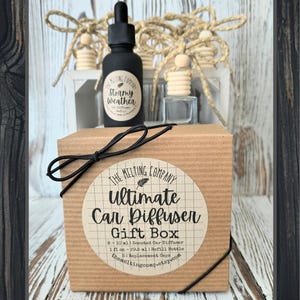 May include: A car air freshener gift box with a black bottle labeled "Stormy Weather" and a clear refill bottle. The box is brown with a black bow and a label that reads "Ultimate Car Diffuser Gift Box". The background includes decorative wooden elements.