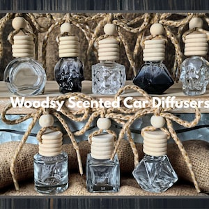 May include: An assortment of car air fresheners with wooden tops and decorative rope accents. The glass bottles come in various shapes, including a skull design. The text "Woodsy Scented Car Diffusers" is displayed on the image.