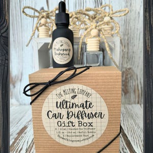 May include: A gift box set containing a black bottle with a dropper, a small clear bottle, and wooden car diffuser ornaments. The box is brown with a black bow and a round label that reads "Ultimate Car Diffuser Gift Box". The set includes a refill bottle.