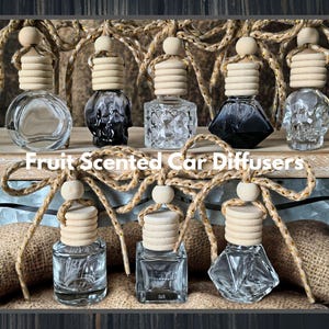 May include: Collection of fruit-scented car diffusers in various clear glass bottle shapes, including a skull design. Each bottle has a wooden cap and is suspended by a decorative rope. The text "Fruit Scented Car Diffusers" is displayed.