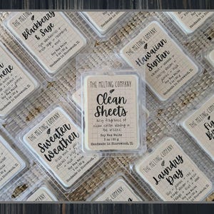 May include: An overhead shot of several soy wax melt packages from The Melting Company. The packages are rectangular with labels featuring various scents like "Clean Sheets," "Blackberry & Sage," and "Hawaiian Suntan." Each package contains 5 oz (142 g) of wax melts.