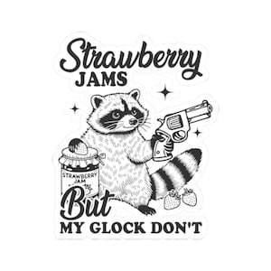Puede incluir: Una ilustración en blanco y negro de un mapache sosteniendo un arma y un frasco de mermelada de fresa. El texto "Strawberry Jams But My Glock Don't" está escrito sobre el mapache.