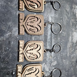 May include: Four wooden keychains with the RAM logo and a silver key ring. Each keychain features a brown and light brown wood design with the RAM logo in the center.