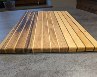 May include: A wooden chopping board with a dark brown and light wood grain pattern. The board is made of multiple strips of wood, creating a striped effect.