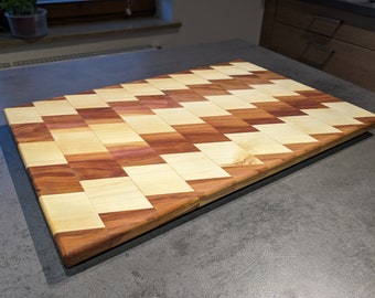 May include: A large, rectangular chopping board made of two different types of wood. The wood is arranged in a chequered pattern, with alternating squares of light and dark wood. The board is made of a light wood and a darker reddish-brown wood.