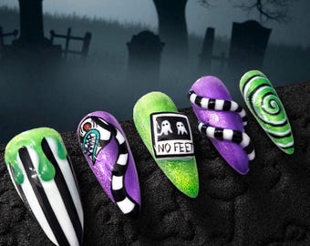 Puede incluir: Un conjunto de cinco uñas postizas en forma de estilete con diseños temáticos de Halloween. Las uñas muestran rayas verticales blancas y negras con baba verde, un gráfico de monstruo, un cuadrado blanco con dos fantasmas y el texto NO FEET, rayas blancas y negras, y un patrón en espiral verde y blanco.