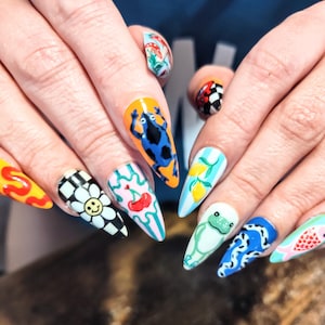 May include: A set of long, almond-shaped, painted nails. Each nail features a unique design, including a frog, cherries, lemons, a daisy, and a checkerboard pattern. The color palette includes bright blues, yellows, greens, and pinks.
