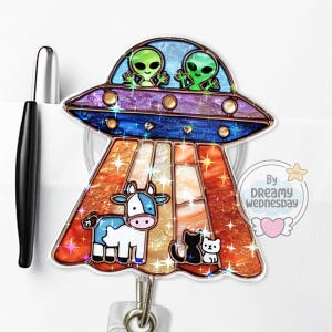 May include: A badge reel featuring a colorful UFO design with two green aliens, a blue and white cow, and two black and white cats. The reel has a retractable cord and a clip for attaching to clothing.
