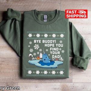 Op de afbeelding: Militairgroen sweatshirt met een narwal-afbeelding en de tekst "Bye Buddy! Hope You Find Your Dad!". Het ontwerp bevat sneeuwvlokken en een winterse scène. De sweatshirt heeft een ronde hals.