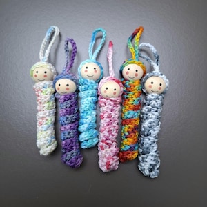 May include: Seven crocheted doll keychains with colorful yarn and wooden heads. The dolls are in various colors, including pink, blue, purple, and orange.