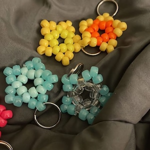 Puede incluir: Un conjunto de cinco llaveros de cuentas de colores. Los llaveros tienen forma de estrellas y flores. Los colores incluyen amarillo, naranja, azul y transparente.