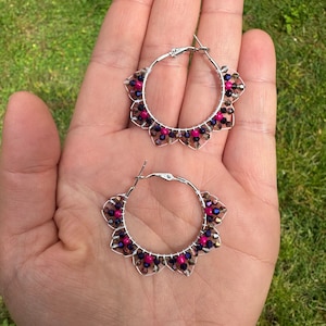 May include: A pair of silver hoop earrings with pink and purple beads. The earrings are made of wire and have a delicate, floral design.
