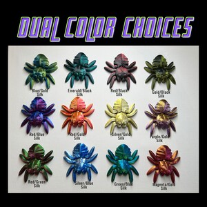 May include: A selection of 12 dual-color spider charms, each with a different color combination. The charms are made of resin and have a shiny, iridescent finish. The colors include blue, gold, emerald, black, red, silver, purple, and magenta.