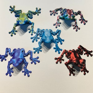 May include: Five small plastic frog figurines in different colors. The frogs are posed in a sitting position with their legs outstretched. The frogs are blue, green, red, and purple.