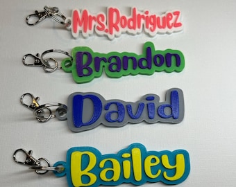 Könnte beinhalten: Vier farbige 3D-gedruckte Schlüsselanhänger mit Namen darauf. Die Schlüsselanhänger sind an silbernen Schlüsselringen befestigt. Die Namen sind "Mrs. Rodriguez", "Brandon", "David" und "Bailey".