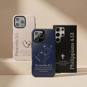 May include: Three phone cases with religious inscriptions. One is light pink with "Proverbs 3:5" and a heart and cross design. Another is navy blue with floral art and the same scripture. The third is black with "Philippians 4:13" and a cross.