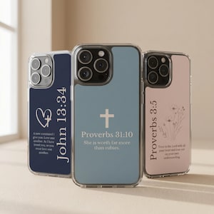 Op de afbeelding: Drie transparante telefoonhoesjes met verschillende ontwerpen. Eén hoesje is marineblauw met een hart en tekst uit Johannes 13:34. Een andere is lichtblauw met een kruis en Spreuken 31:10. De derde is roze met Spreuken 3:5.