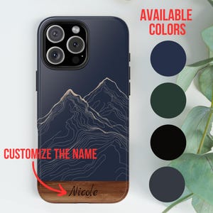 May include: A personalised phone case featuring a mountain range design in white lines on a dark blue background. The case has a wood accent at the bottom with the name "Nicole" written in cursive. The case is available in four colours: navy blue, dark green, black, and light blue.