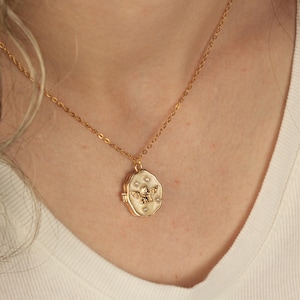 May include: A gold chain necklace with a white oval locket featuring a gold angel with wings and small clear rhinestones.