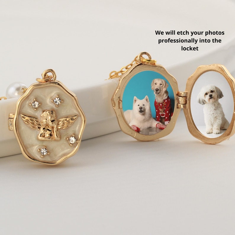 May include: Gold locket necklace with a white enamel angel design on one side and a photo of two dogs on the other side. The locket is open and the photo is visible. The text "We will etch your photos professionally into the locket" is visible in the image.