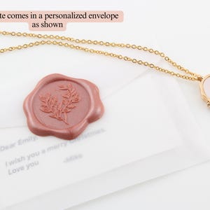 May include: A gold chain necklace with a white and gold locket featuring a butterfly design. The necklace is packaged in a white envelope with a red wax seal.
