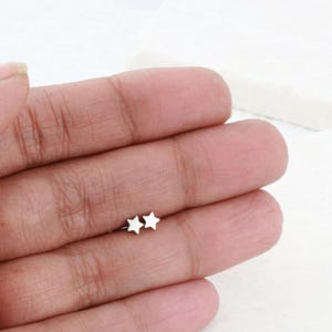 May include: A pair of silver star-shaped stud earrings. The earrings are small and delicate, and they are shown on a person's hand.