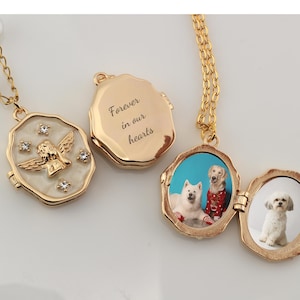 May include: Gold locket necklace with a photo of two dogs inside. The locket has a separate compartment with an angel design and rhinestones. The back of the locket is engraved with the words "Forever in our hearts".