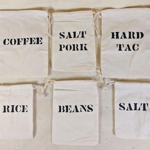 May include: Six off-white canvas drawstring bags, each labeled in bold black letters. The bags are labeled: "COFFEE", "SALT PORK", "HARD TAC", "RICE", "BEANS", and "SALT". The bags are arranged in two rows of three.
