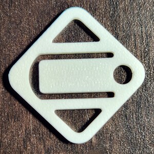 May include: White plastic key chain with a diamond shape and a cut-out design. The key chain has a small hole for attaching keys.
