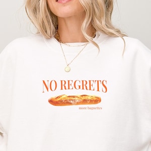May include: White sweatshirt with the text "NO REGRETS" and a drawing of a baguette with the text "more baguettes" underneath.