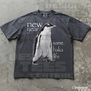 May include: Dark gray t-shirt featuring a black and white penguin illustration. The text on the shirt reads "new year same baka life". The shirt is a casual wear item.