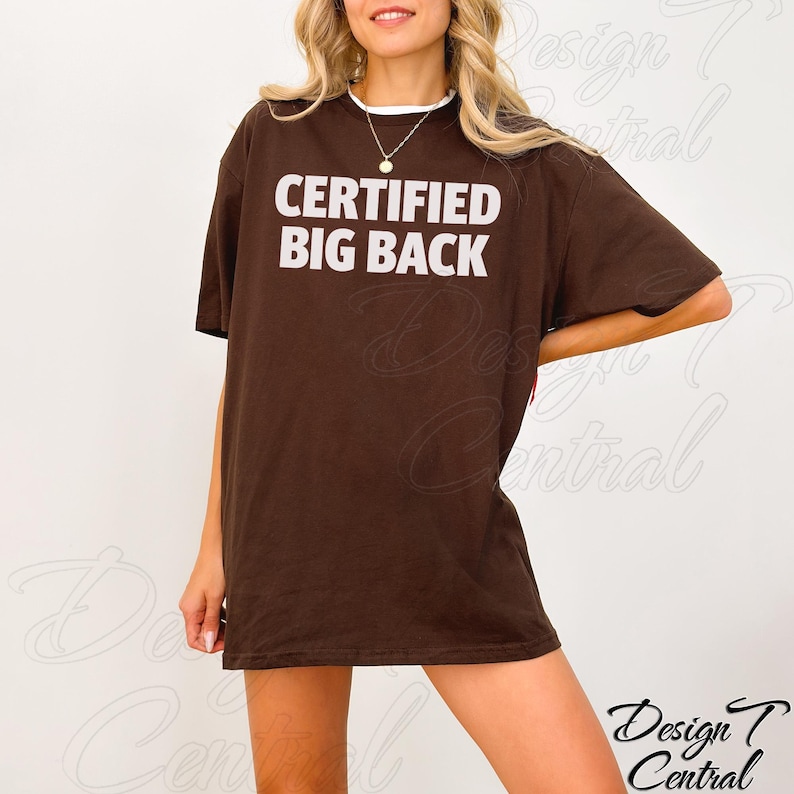 May include: A brown t-shirt with the text "CERTIFIED BIG BACK" in white block letters. The shirt has a white collar and short sleeves. The model is wearing the shirt.