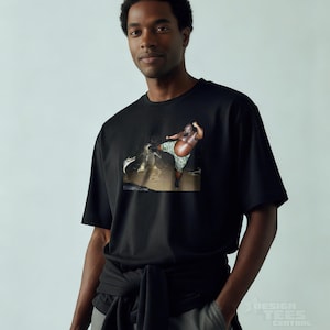 May include: Black t-shirt featuring a colorful graphic print. The graphic depicts a person in a body of water. The shirt is made of a soft material and has short sleeves. The shirt is being worn by a person.