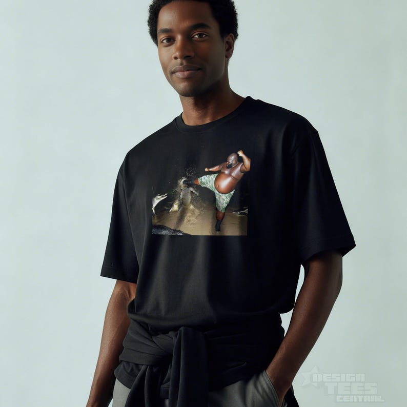 May include: Black t-shirt featuring a colorful graphic print. The graphic depicts a person in a body of water. The shirt is made of a soft material and has short sleeves. The shirt is being worn by a person.