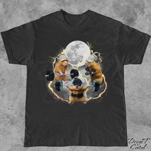 May include: Black t-shirt featuring a humorous graphic of three hamsters weightlifting. The hamsters are wearing hats and headphones, with a full moon and lightning in the background. The shirt has the text "Design Central" at the bottom.