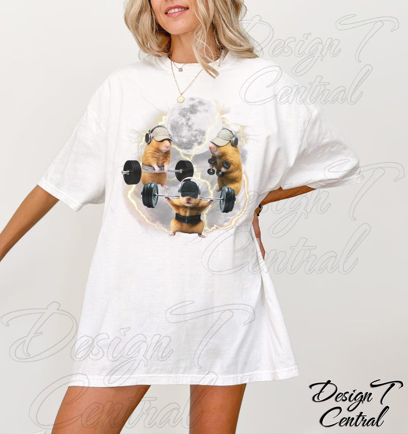 May include: White t-shirt featuring a whimsical design of three hamsters lifting weights under a full moon. The hamsters wear hats and headphones, with a lightning bolt effect around them. The shirt has a relaxed fit.