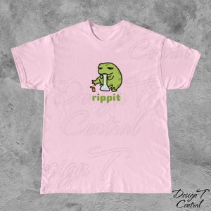May include: A pink t-shirt with a cartoon frog smoking a bong. The frog is green and has a relaxed expression. The text "rippit" is printed below the frog.