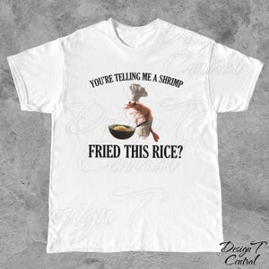May include: White t-shirt with a funny graphic of a shrimp wearing a chef's hat and holding a pan of fried rice. The text on the shirt reads "You're telling me a shrimp fried this rice?"