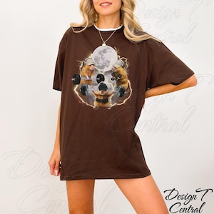 May include: A brown t-shirt featuring a graphic of hamsters weightlifting under a full moon. The hamsters are wearing hats and headphones. The text "Design Central" is in the lower right corner.