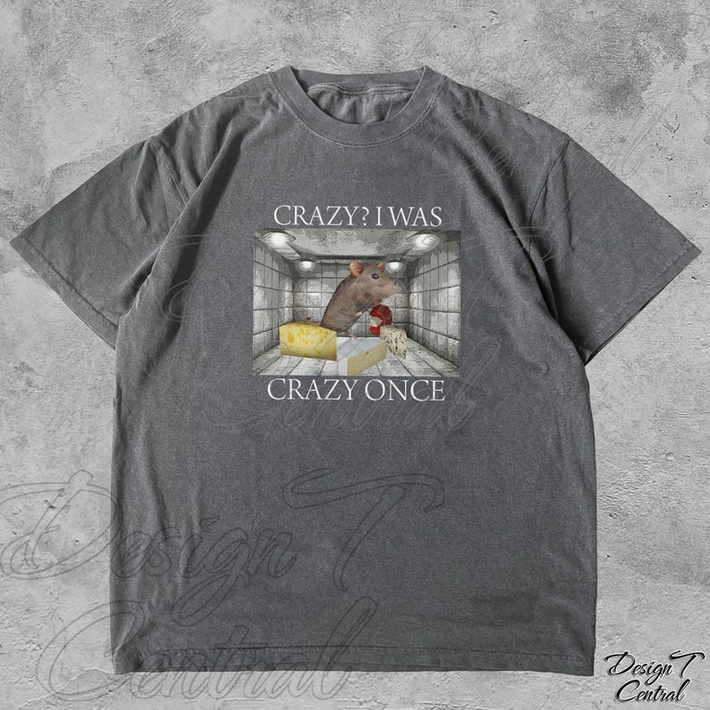 Puede incluir: Camiseta gris con un gr&aacute;fico de una rata en una jaula, queso y el texto "Crazy? I was crazy once". La rata lleva un guante de boxeo rojo. La camiseta tiene un corte holgado y est&aacute; hecha de material suave.