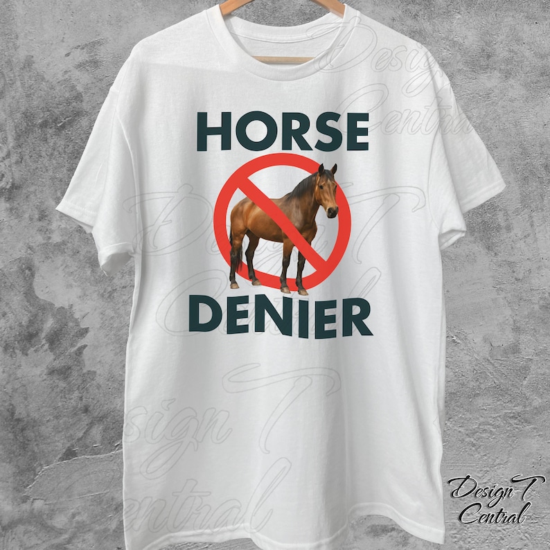Peut inclure: T-shirt blanc avec l'inscription "HORSE DENIER" en lettres majuscules vert fonc&eacute;. Un cheval marron est &agrave; l'int&eacute;rieur d'un cercle rouge barr&eacute;. Le t-shirt est suspendu &agrave; un cintre blanc.