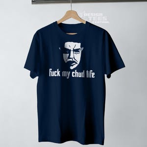 May include: Navy blue t-shirt with a white graphic of a face wearing glasses and the text "fuck my chud life". The shirt is hanging on a wooden hanger.